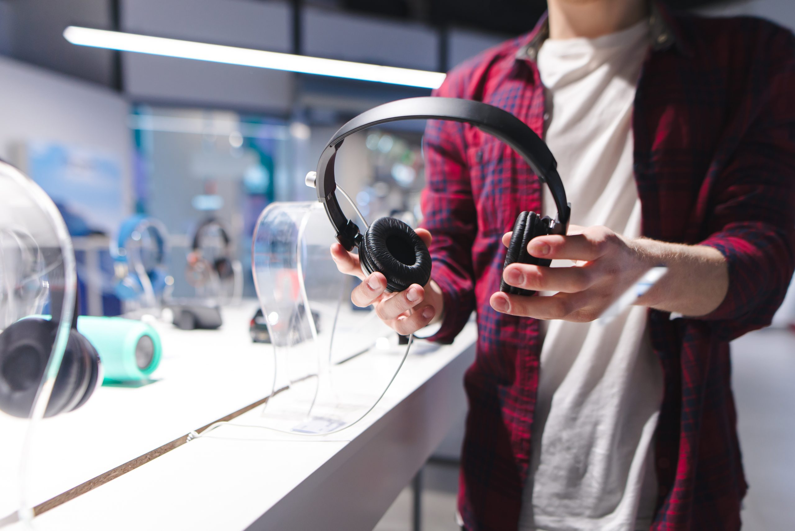 A man holds black headphones in the background of the store. Buying headphones in a tech store.